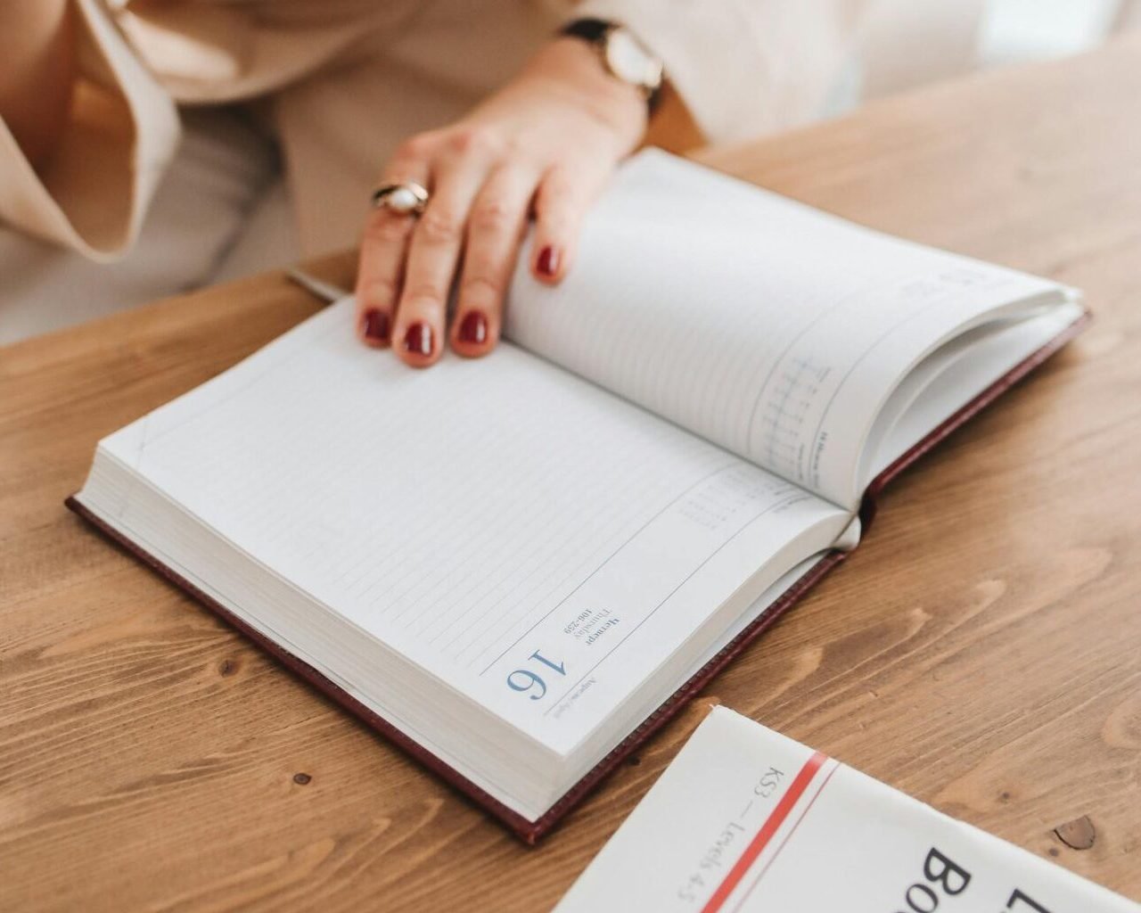 Adult woman writing in an open notebook at a wooden desk, focusing on reading and note-taking.