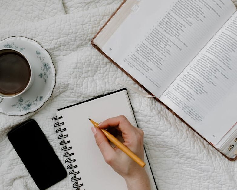Handwriting on notebook with open book and coffee in bed. Perfect cozy setup for reading or studying.