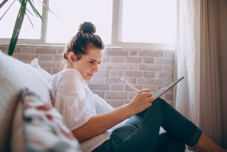 A young woman focused on remote work using a tablet in a cozy living room.