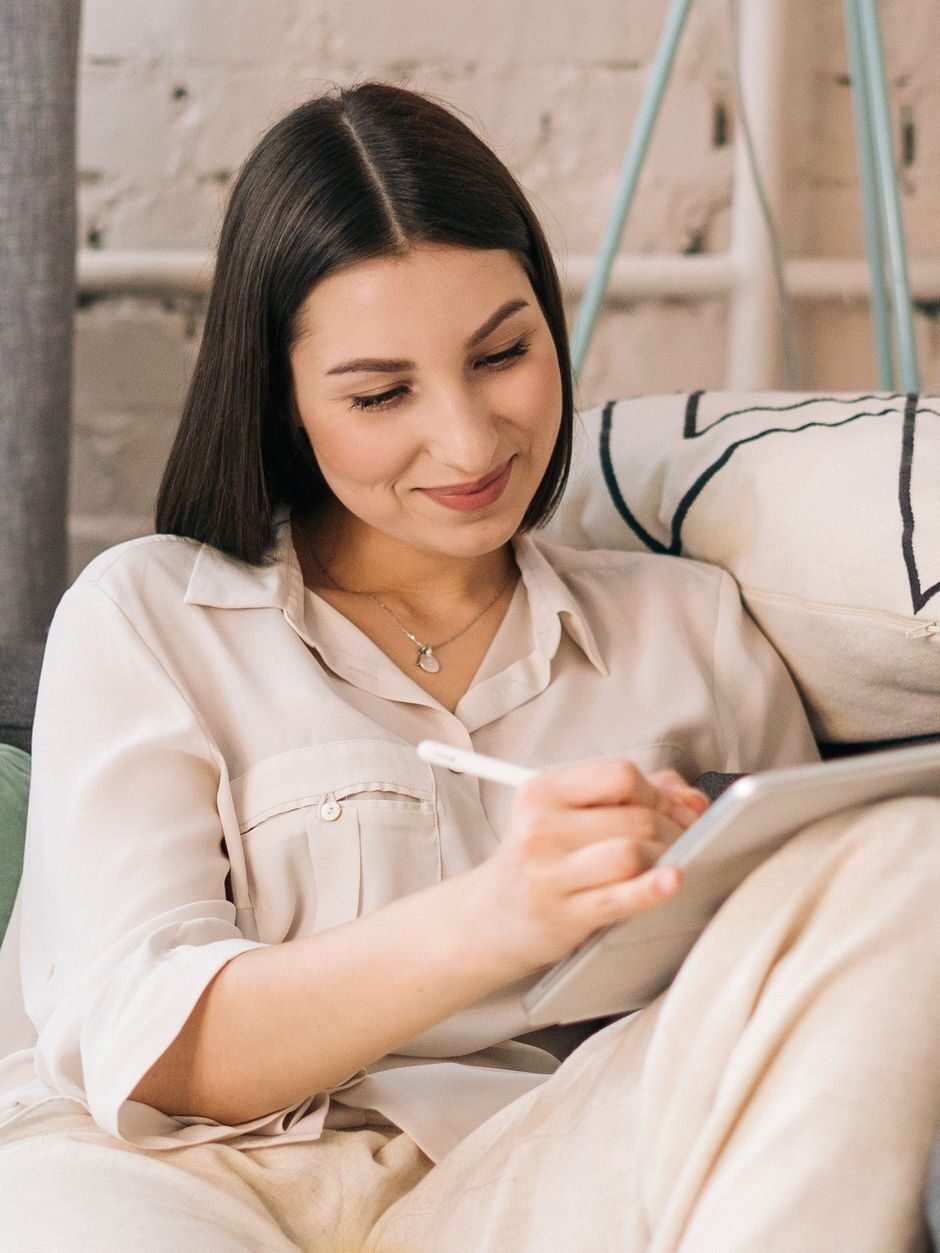 Smiling woman using tablet on sofa in a cozy home setting, enjoying work from home.